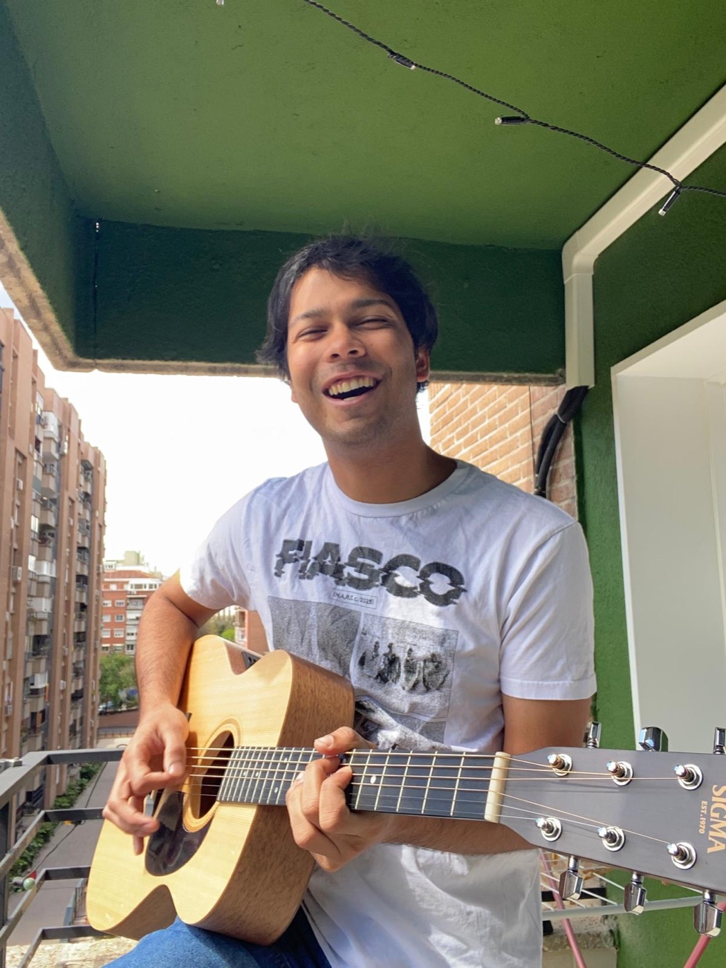 weyvir laughing with an acoustic guitar on a Madrid balcony